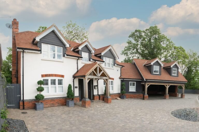 Block-paved driveway in front of a white-rendered house with dormer windows, an oak porch and a car port
