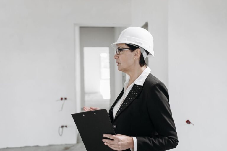 Woman in a white hard hat holding a clipboard while inspecting an unfinished room with bare walls
