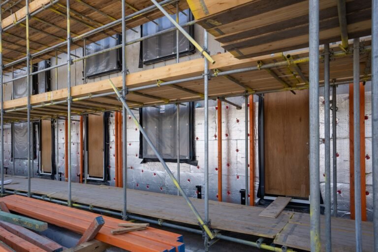 Scaffolding in front of a house wall covered in foil-faced insulation boards held with red fixings