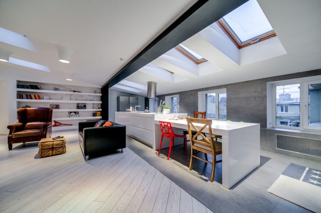 Open-plan kitchen with a long white island under a row of rooflights and an exposed black steel beam
