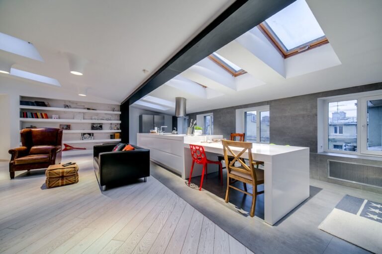 Open-plan kitchen with a long white island under a row of rooflights and an exposed black steel beam