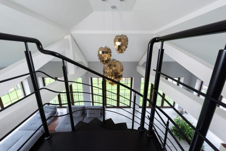 View down an open black staircase with curved metal handrails from an upper floor into a bright lounge