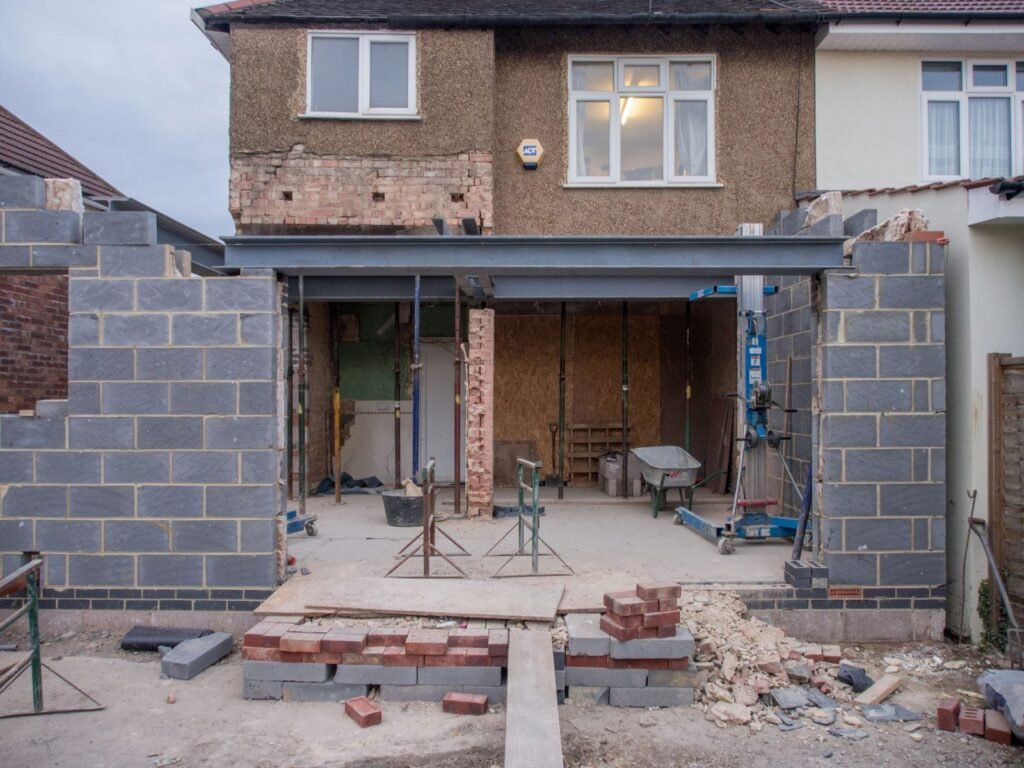 Rear extension under construction on a pebbledashed semi-detached house, with blockwork walls and a steel beam
