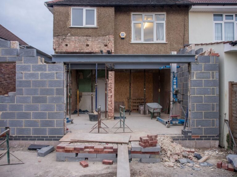 Rear extension under construction on a pebbledashed semi-detached house, with blockwork walls and a steel beam