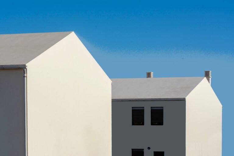 Two gable-fronted houses finished in smooth cream and dark grey render against a clear blue sky