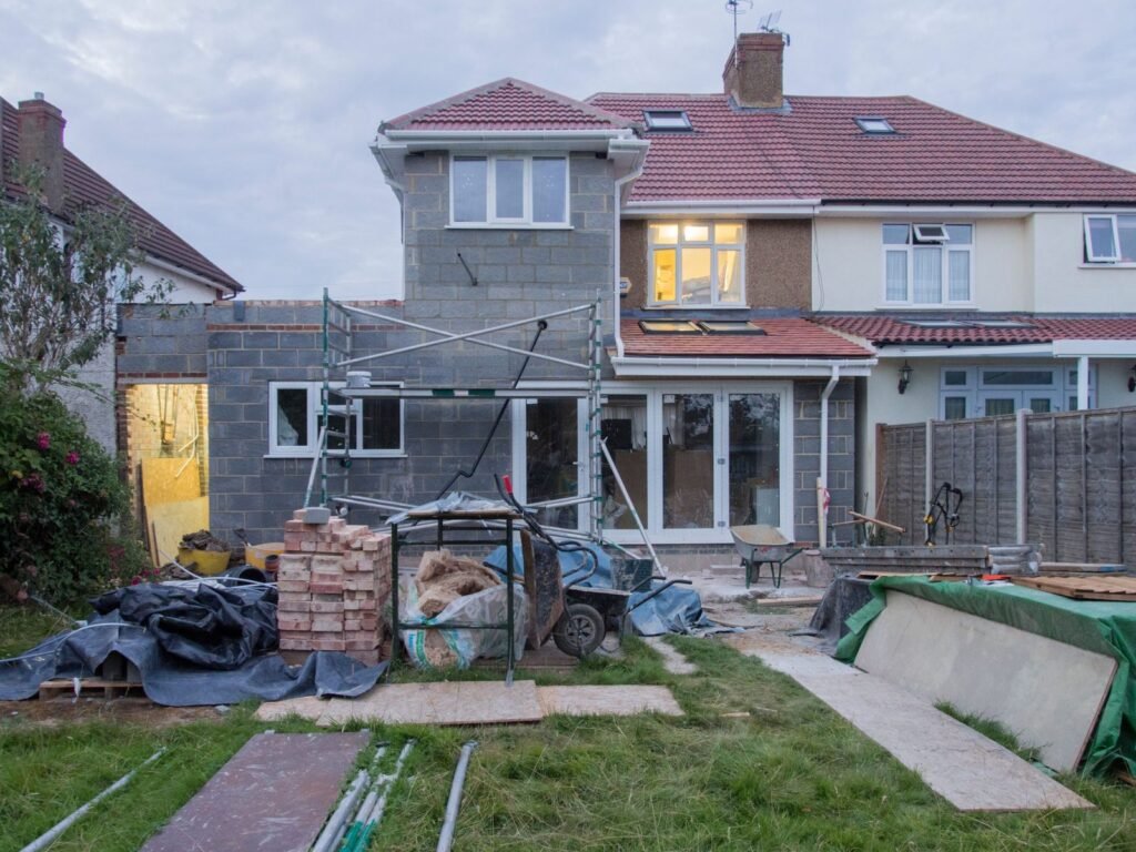Rear of a semi-detached house with a single-storey blockwork extension going up, scaffolding and materials on the lawn