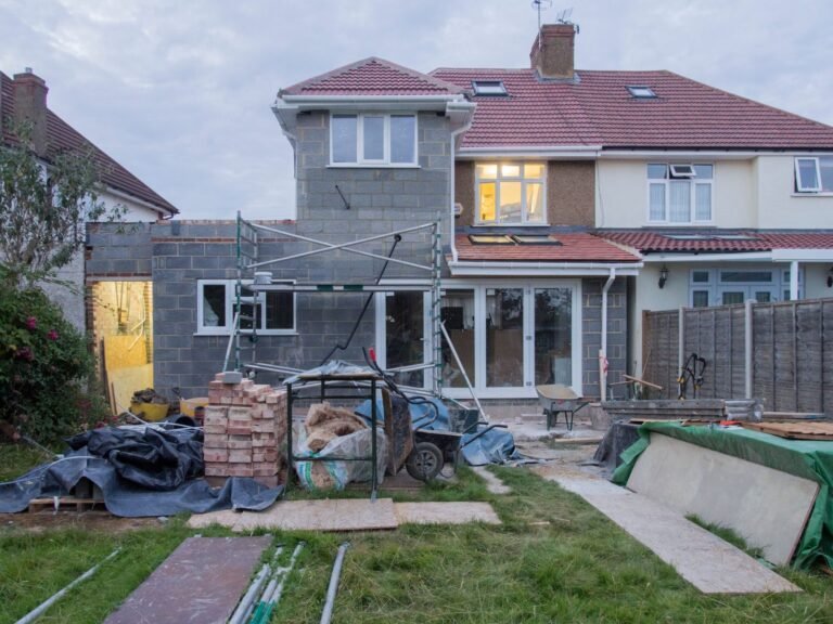 Rear of a semi-detached house with a single-storey blockwork extension going up, scaffolding and materials on the lawn